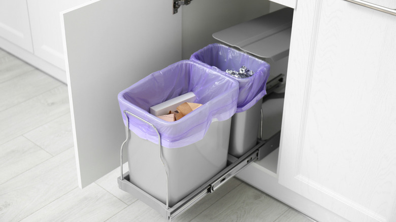 Open cabinet with full trash bins for separate waste collection in kitchen