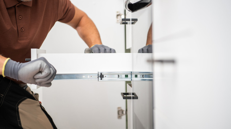 A professional is installing sliding drawers in a cabinet in a contemporary kitchen.