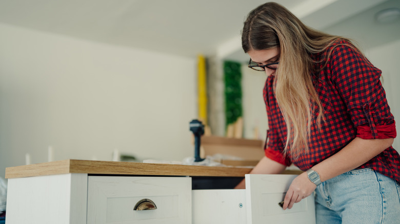 A woman looks inside of a kitchen drawer.