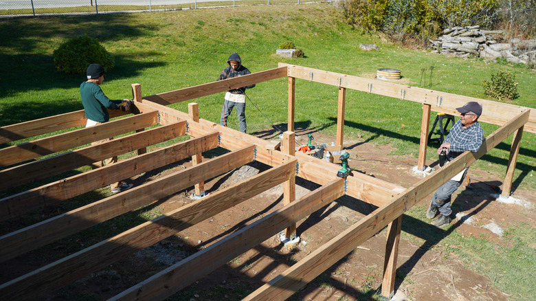 Construction workers building the frame of a deck in a large backyard.
