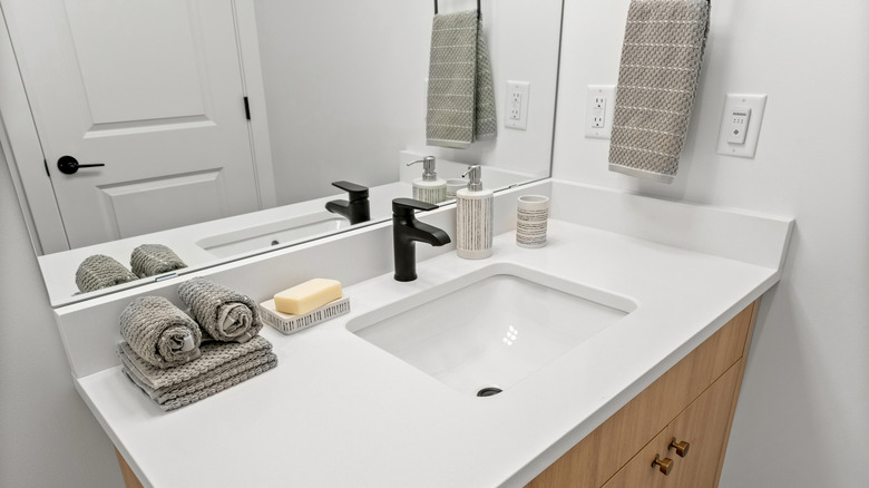A bathroom counter with towels folded and hanging on the wall
