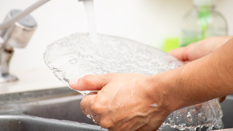 A person hand washes a vintage glass plate with soap and water.