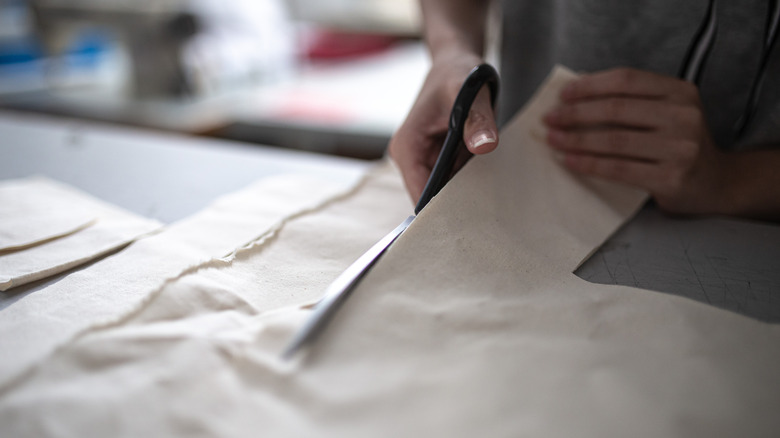 A person cutting strips of white fabric with scissors