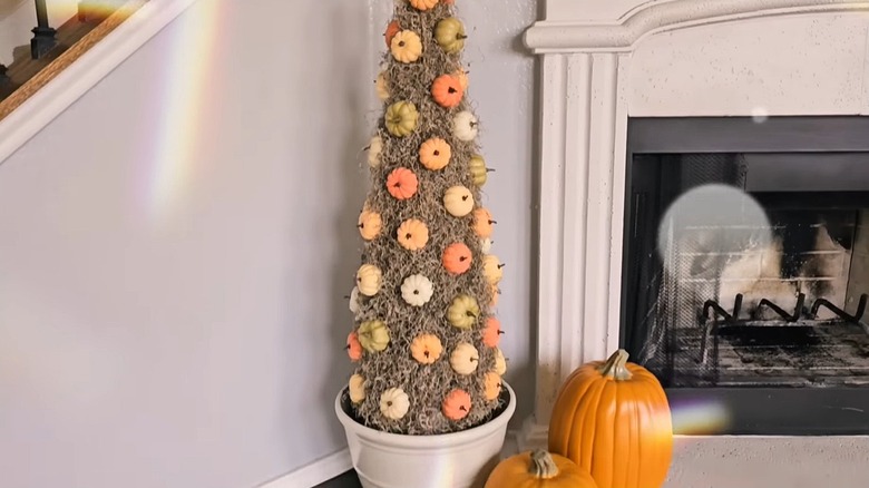 Decorative tree made out of moss and small pumpkins next to a fireplace.