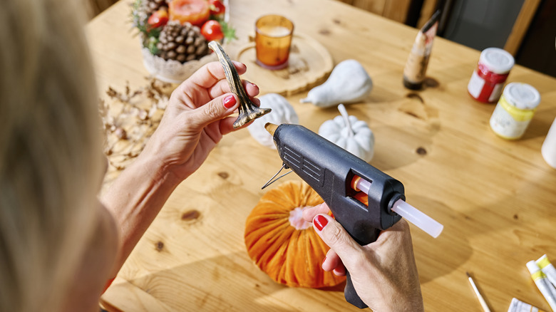 Woman uses hot glue gun to make pumpkin-themed decor for Halloween or fall.