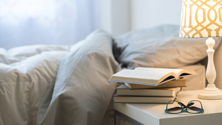 Books rest on a bedside table by an unmade bed