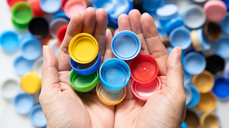 Hands holding different colored bottle caps, with more caps in the background