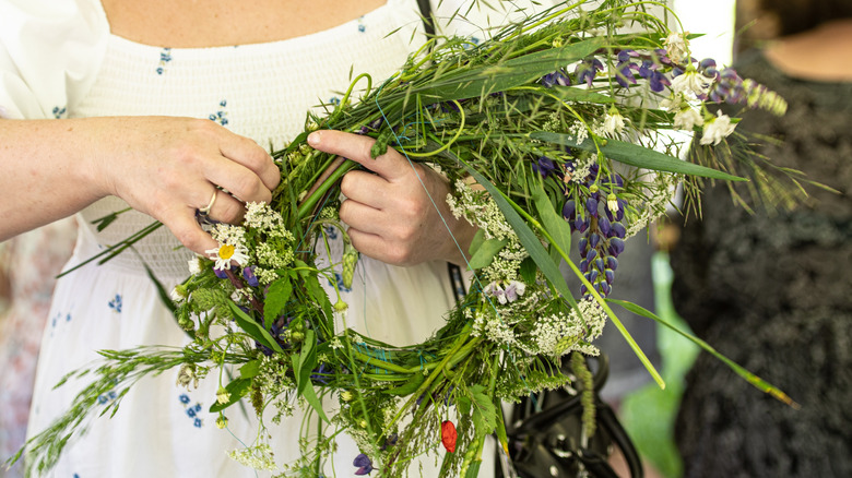 A woman carries flowers and plants twisted in a circle like a wreath or crown.