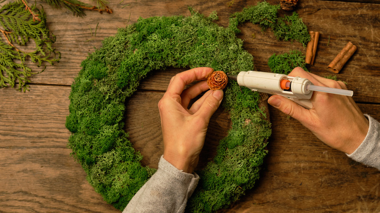 person gluing acorns onto a moss-covered wreath
