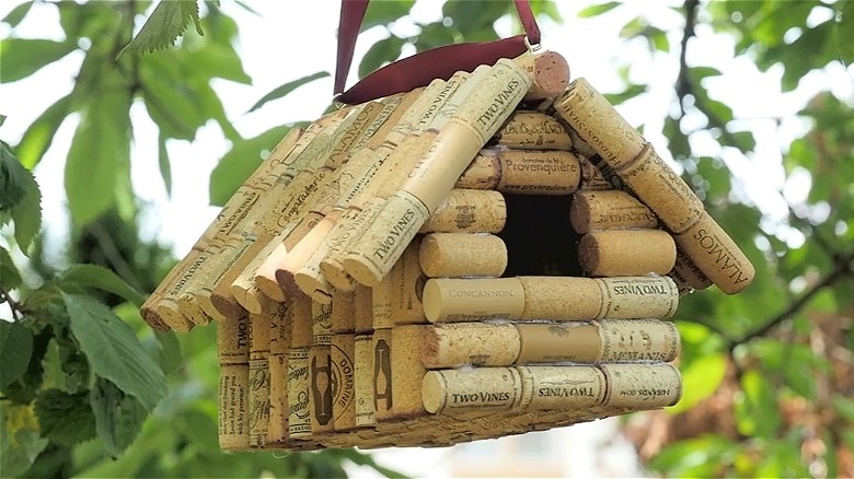 Birdhouse made from wine corks hanging in green leaves.
