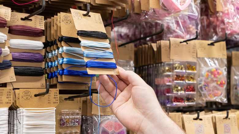 A person reaches for craft supplies hanging on the wall in a store.