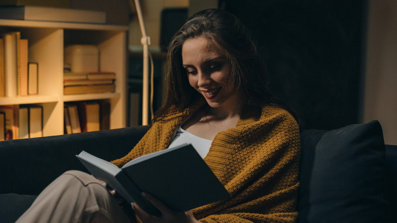A woman reads a book on a sofa while illuminated by moody, ambient lighting