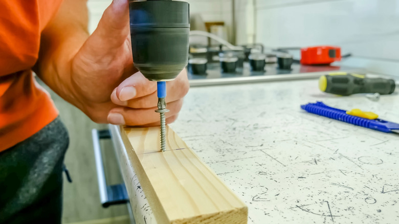 A carpenter uses a power drill to screw into a 1x1 piece of lumber