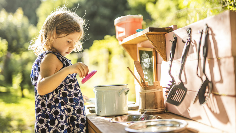 Girl playing in a mud kitchen in her backyard.