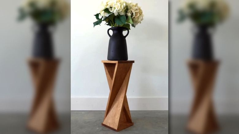 A narrow, twisty table with a flower vase sitting on top.