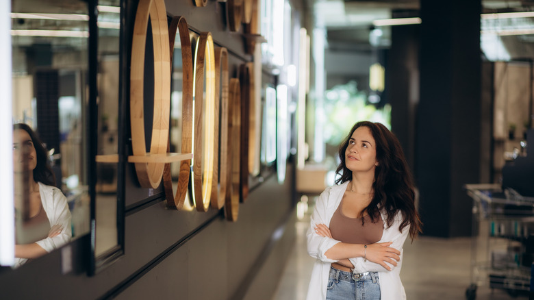 brunette choosing a mirror from a wall displaying different mirrors