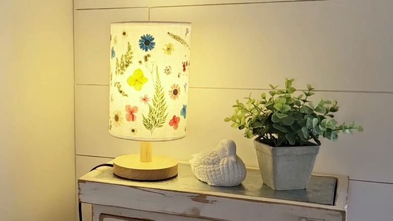 A finished pressed flower lampshade DIY lights up the corner of a room.