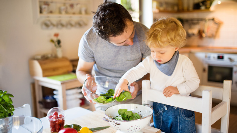 toddler standing on stool in kitchen with parent