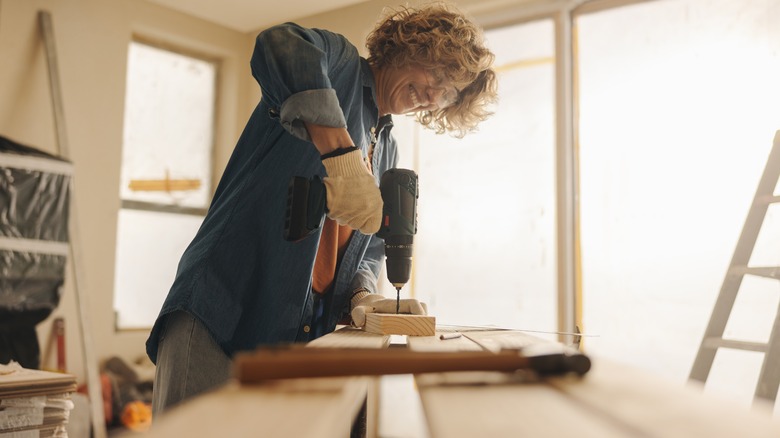 A woman holds a drill and works on a DIY wood project