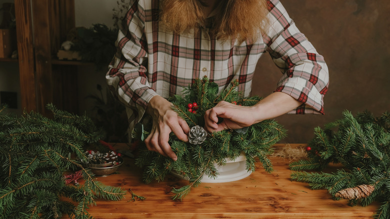 A woman arranges green spruce cuttings into an arrangement