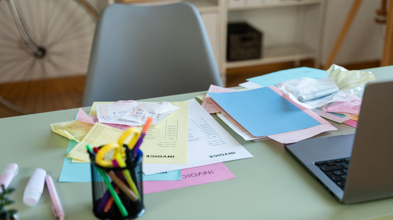 A messy desk with different colorful pieces of paper piled and scattered on it.