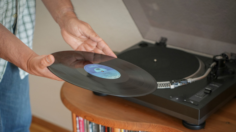 Person wearing striped shirt holding record in two hands above a record player