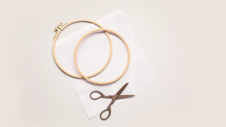 Two wooden embroidery hoops with canvas and scissors on grey background