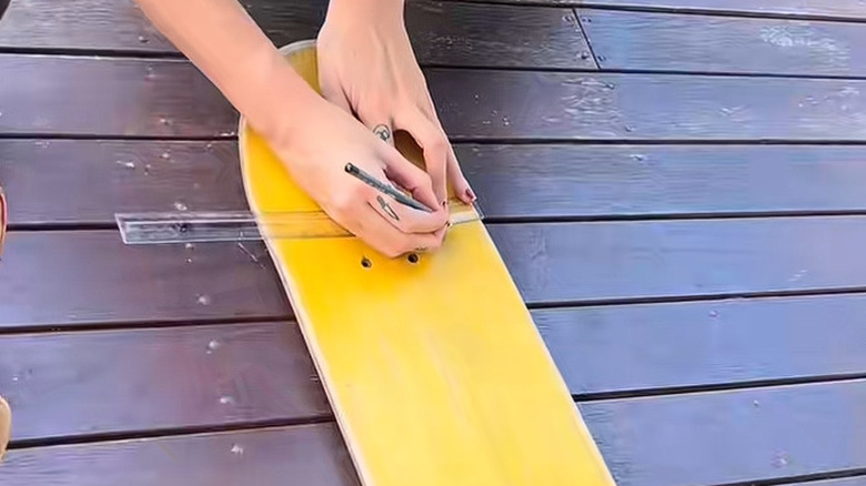 Person using a ruler to mark spots to drill on the end of a yellow skateboard.