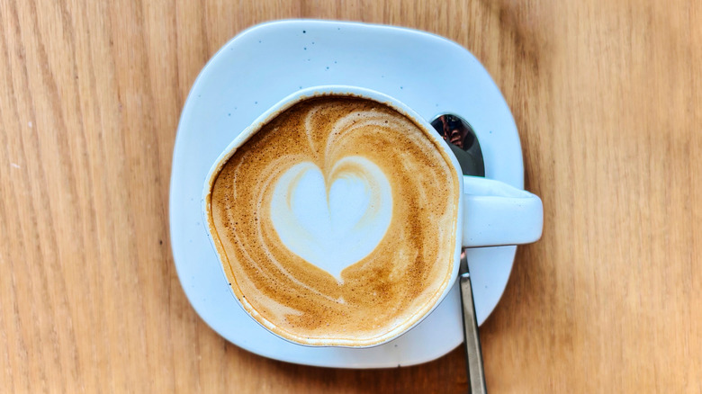 A cup of coffee with heart-shaped foam in the middle.
