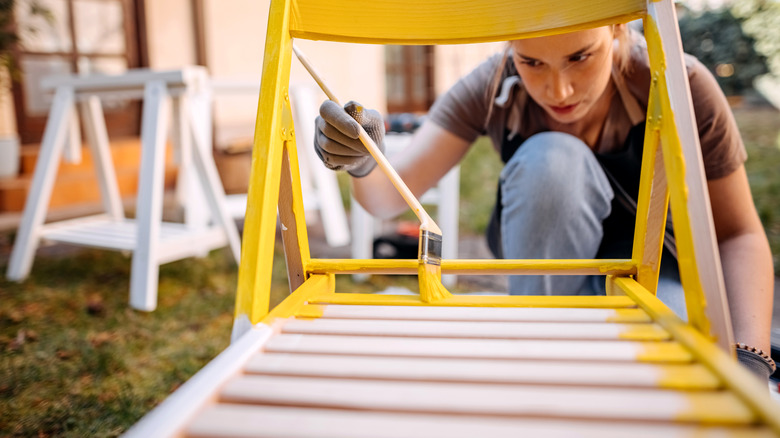 Person painting wood furniture yellow outside