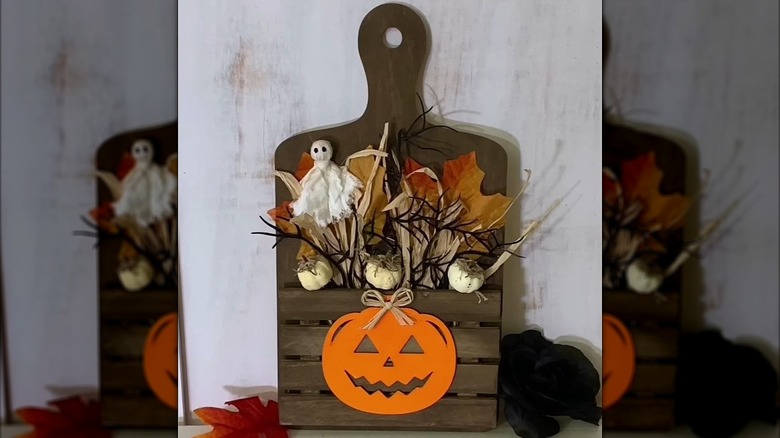 A decorative Halloween wooden tray with a pumpkin, ghosts, and dead leaves attached.