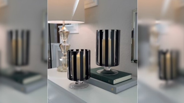 Two glass vases with black vertical stripes holding candles
