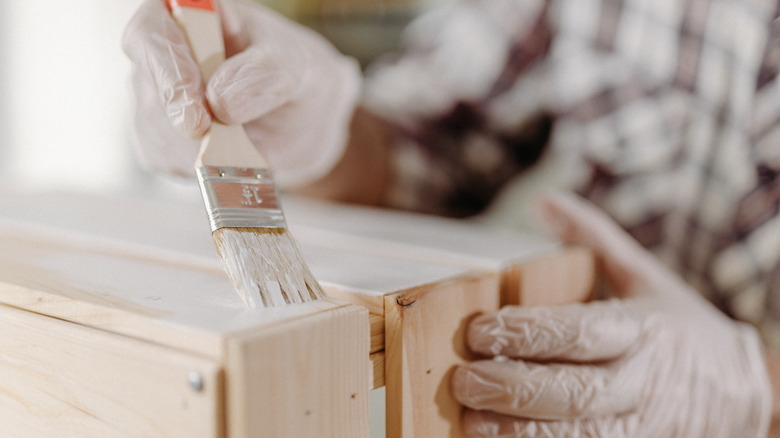 person wearing gloves and holding paint brush painting wood planter