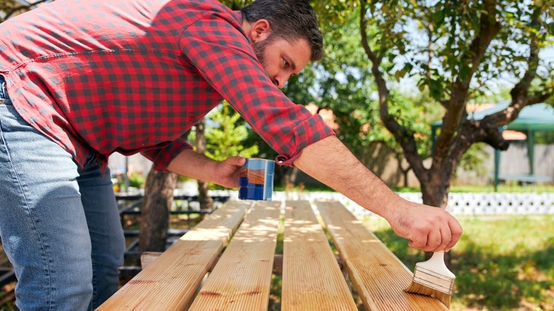 man in red checkered shirt brushing varnish on wood planks outside