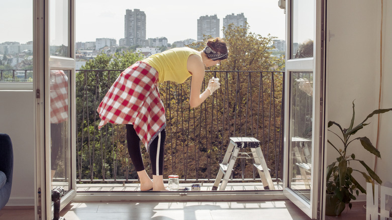 A person stands on a small balcony in the city while cleaning the balustrade