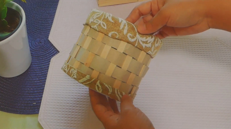 A basket made out of toilet paper rolls, wooden sticks, and fabric.