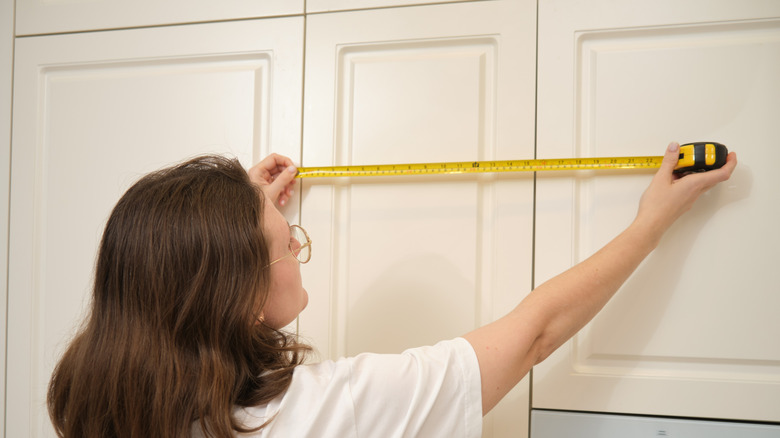 Woman measuring a kitchen cabinet with a measuring tape