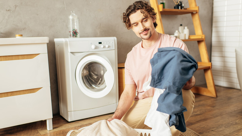 A man smiles as he holds a laundry bag in front of a washing machine.