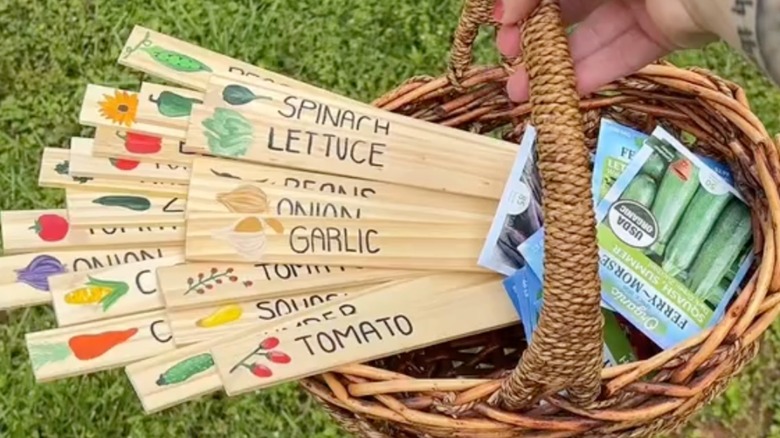 Colorful wooden labels with vegetable names written on them in a basket alongside some packets of seeds