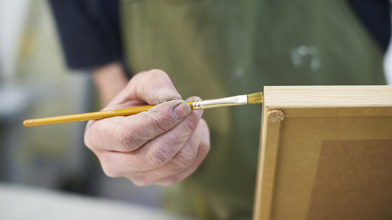 A light-skinned hand paints a wooden picture frame.