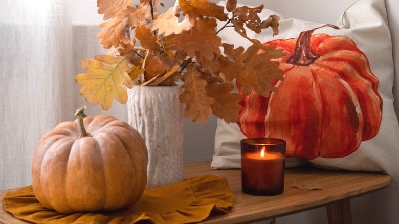 Pumpkin, candle, plant, and fall-themed pillow on small table