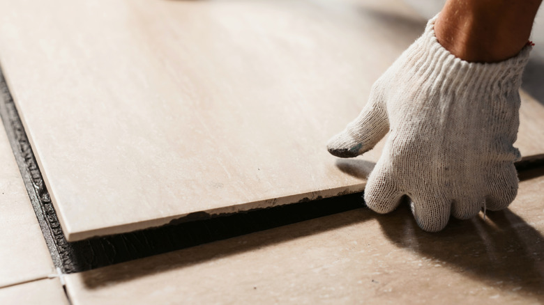 Person laying ceramic tile over a concrete floor
