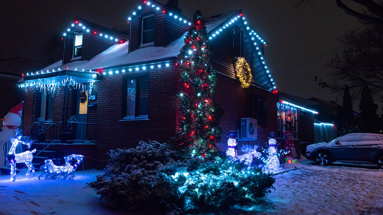 A snowy, brick house is festive with Christmas lights at night