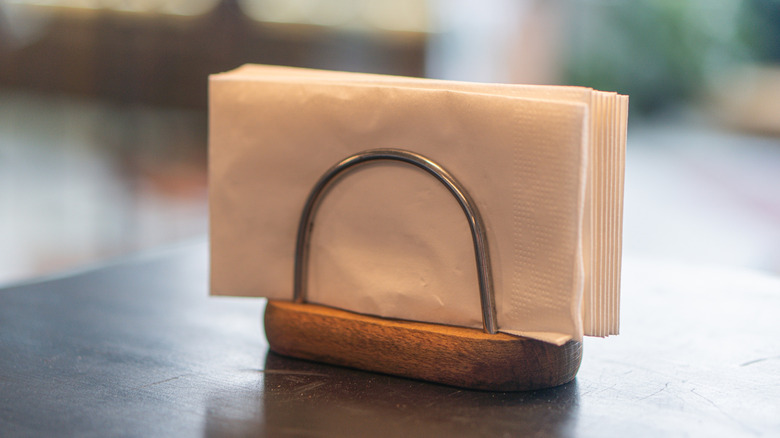 A simple napkin holder holds a stack of white napkins.