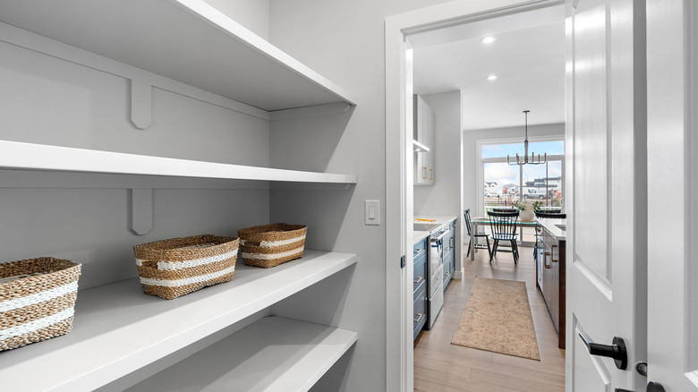 Empty shelves in a pantry with an open door that looks into the kitchen