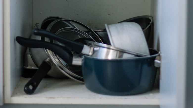 Metal pots and pans with black handles that are disheveled in a white cabinet