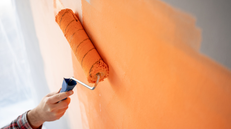 Close-up of decorator's hand painting wall with roller.