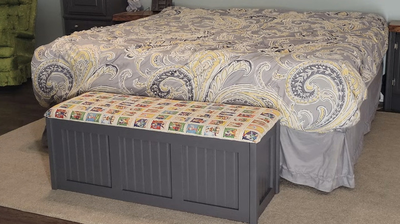 A paisley bed spread on a bed with a storage bench set at the foot of the bed.
