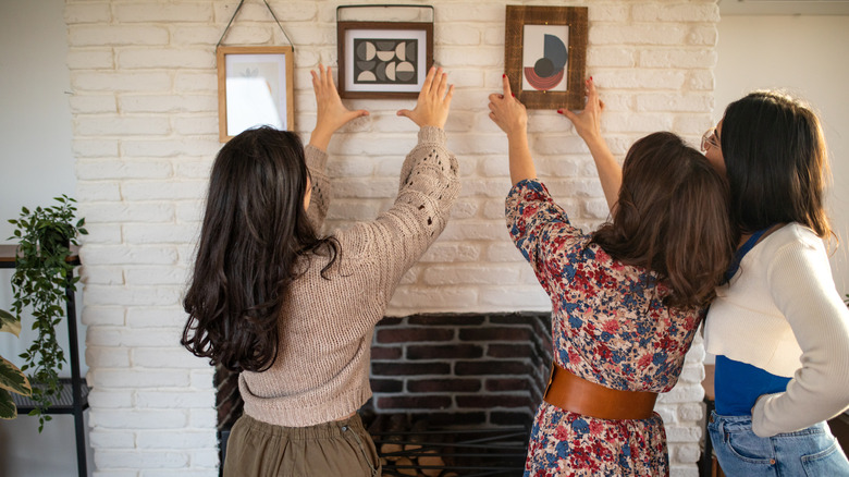 Three women hanging up picture frames.