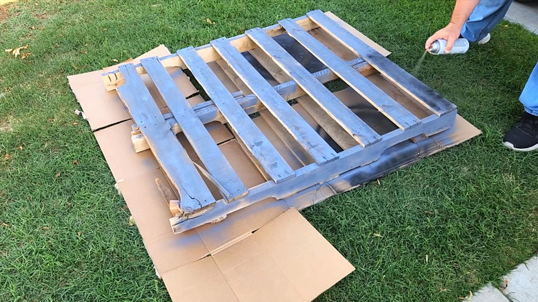 A person spray painting a pallet in their yard.